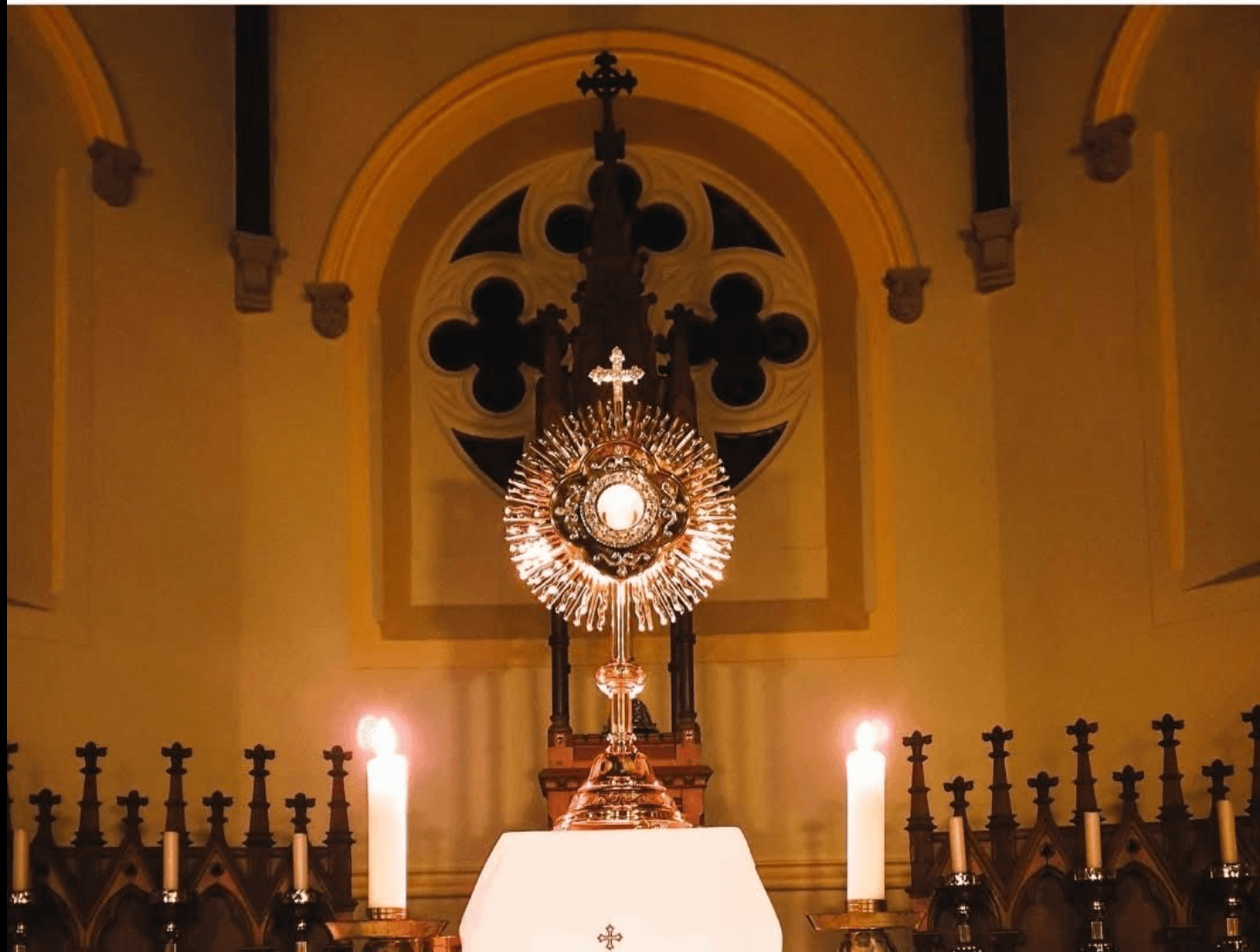 A monstrance in candlelight before the quatrefoil rose window at St Patrick's, Gortin.